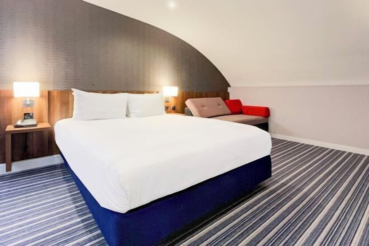 Une chambre d’hôtel avec un grand lit, deux tables de chevet et un mur incurvé.