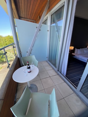 Ein Balkon mit Tisch, Stühlen, einer Weinflasche und einem Glas.