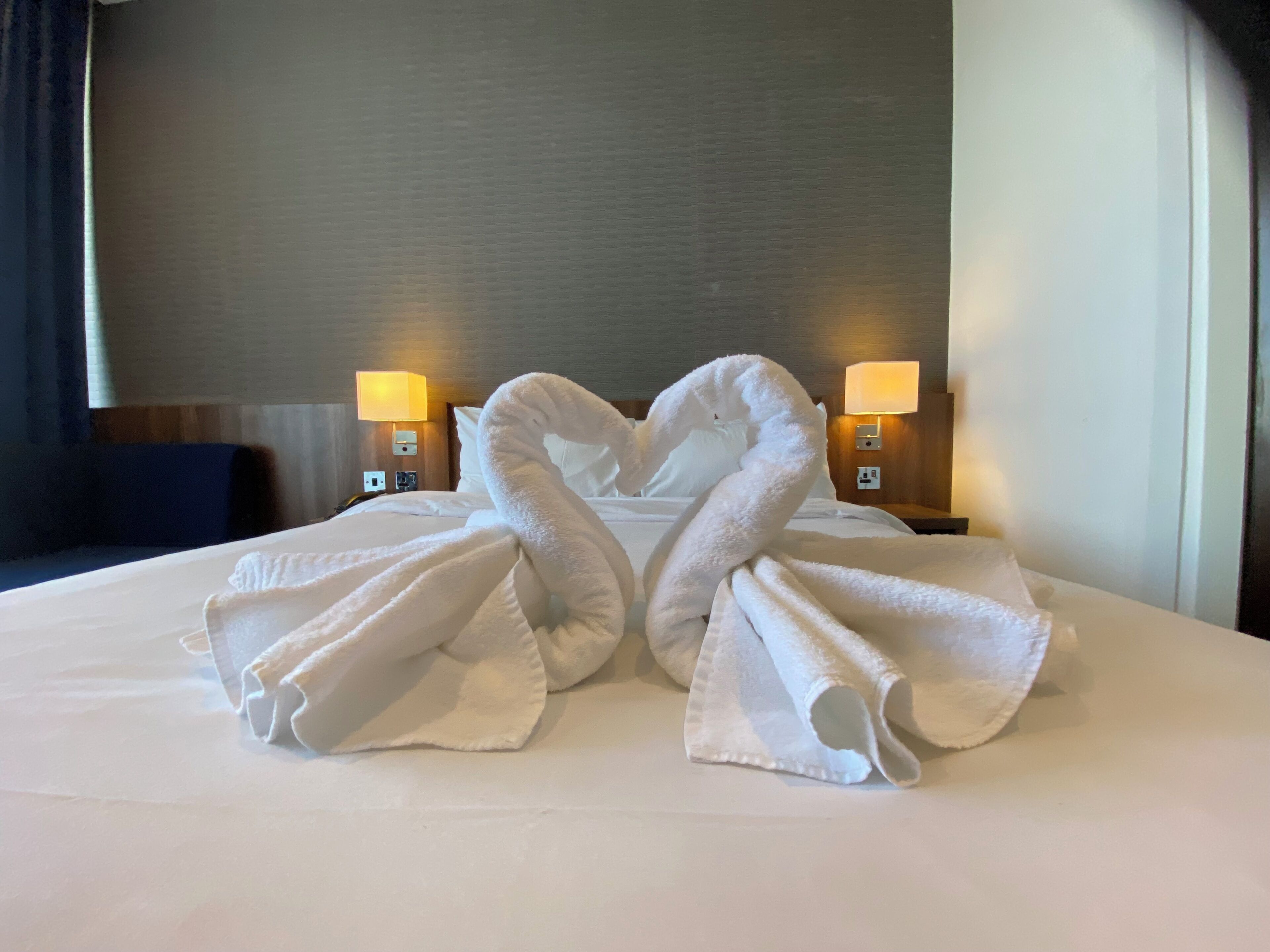 Habitación de hotel con una cama bien hecha, dos lámparas de noche y una luz empotrada en la pared.