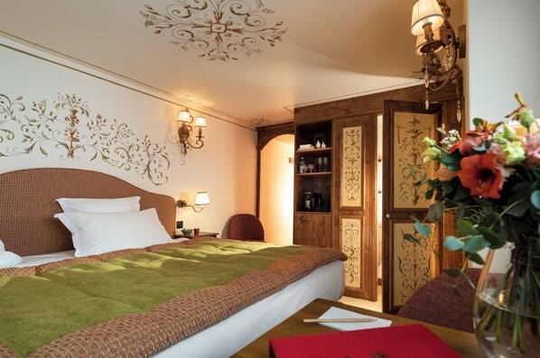 A hotel room with a neatly made bed, a wooden wardrobe, a nightstand with a lamp, and a vase with flowers on the table. - Hotel de la Loze (Courchevel)