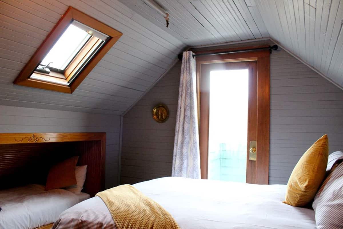 A bedroom with a sloped ceiling, a skylight, a door with a view, and a bed with pillows.
