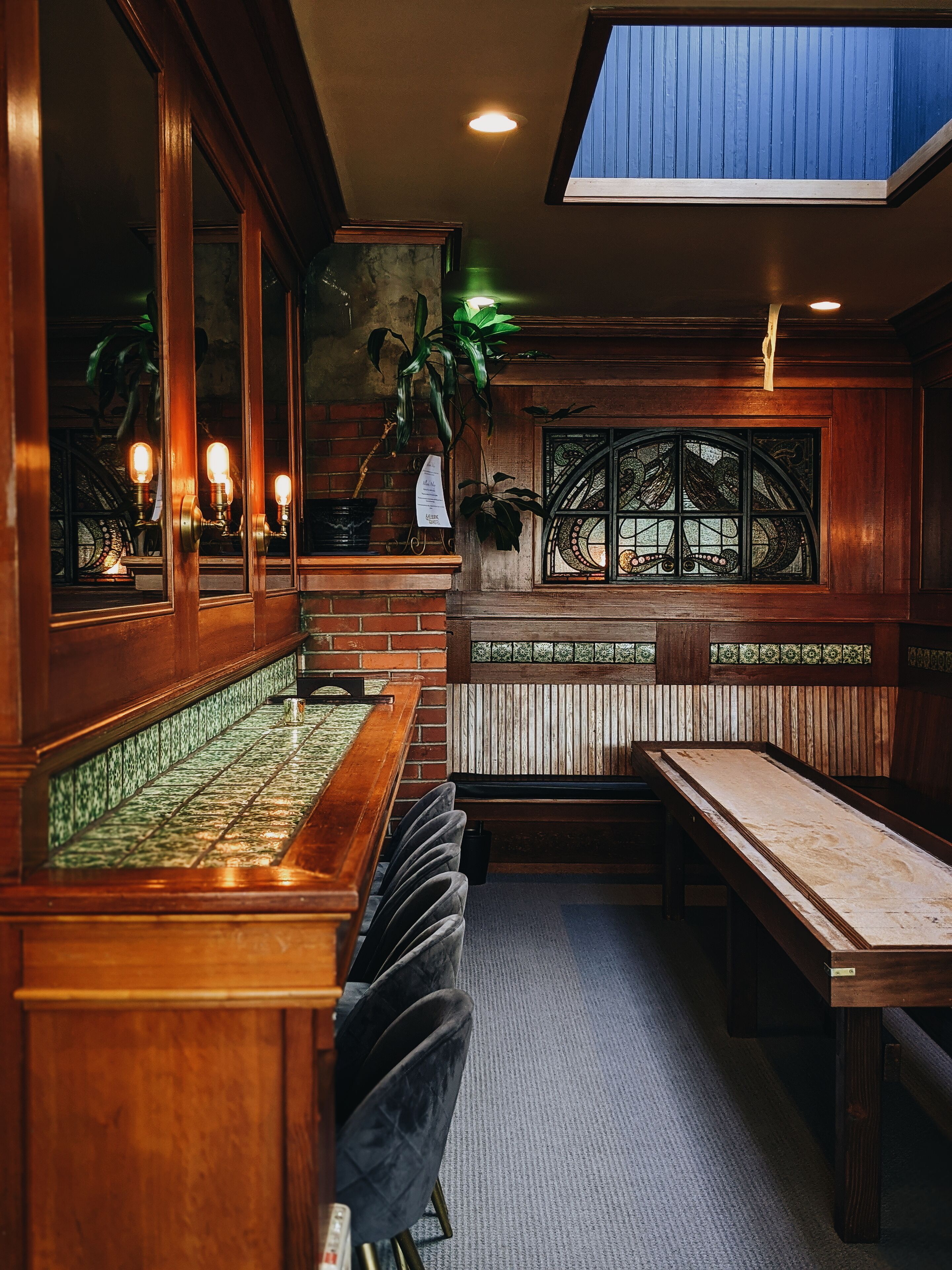 A bar area with wooden bar counter, cushioned bar stools, and a decorative window with stained glass.