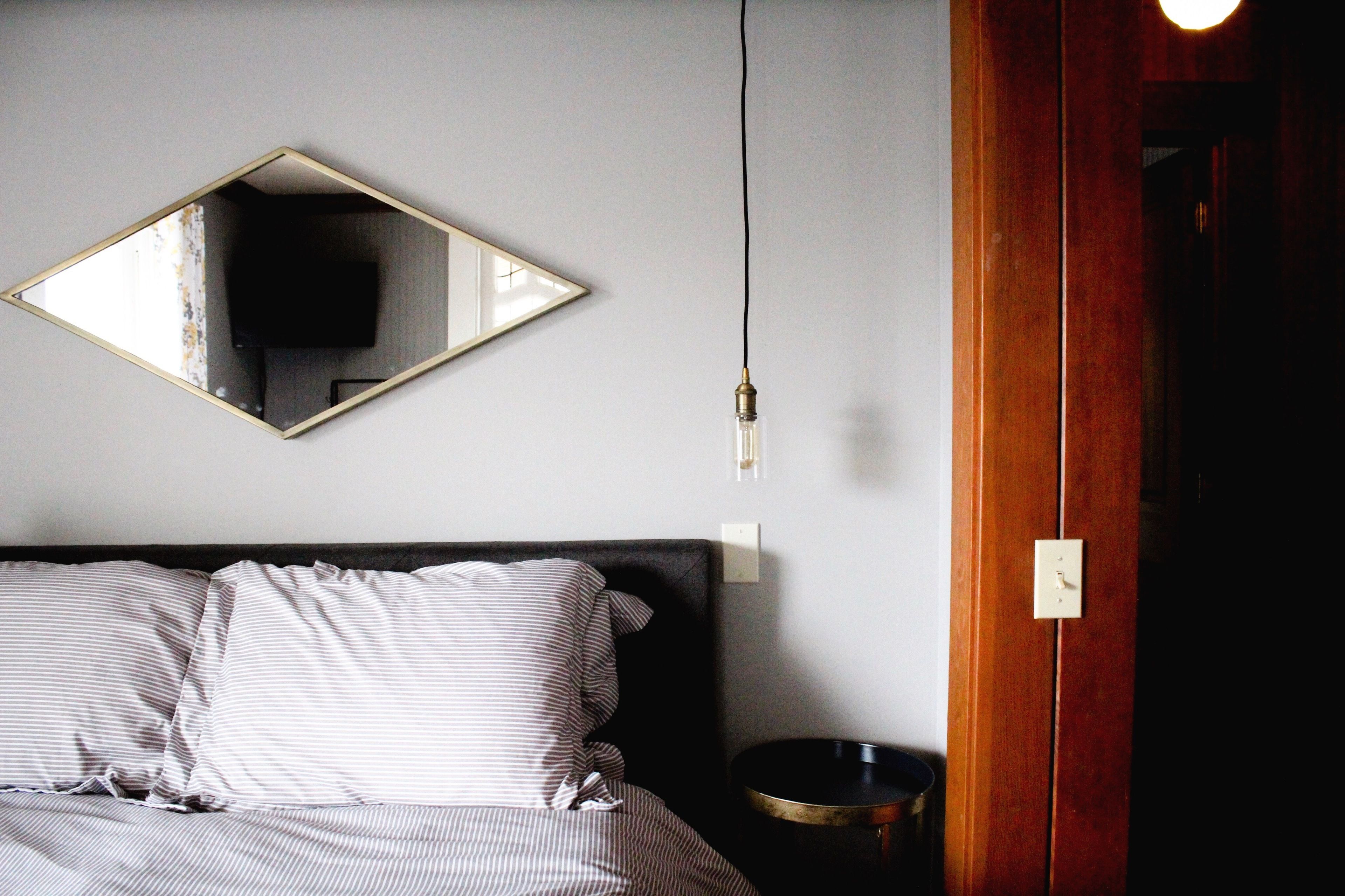 Un dormitorio con cama, mesita de noche, espejo y toma de corriente.