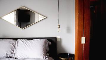 Un dormitorio con cama, mesita de noche, espejo y toma de corriente.