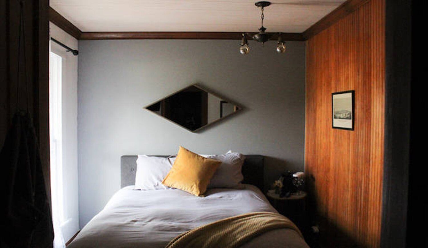 Un dormitorio con cama, mesita de noche, espejo y un cuadro en la pared.