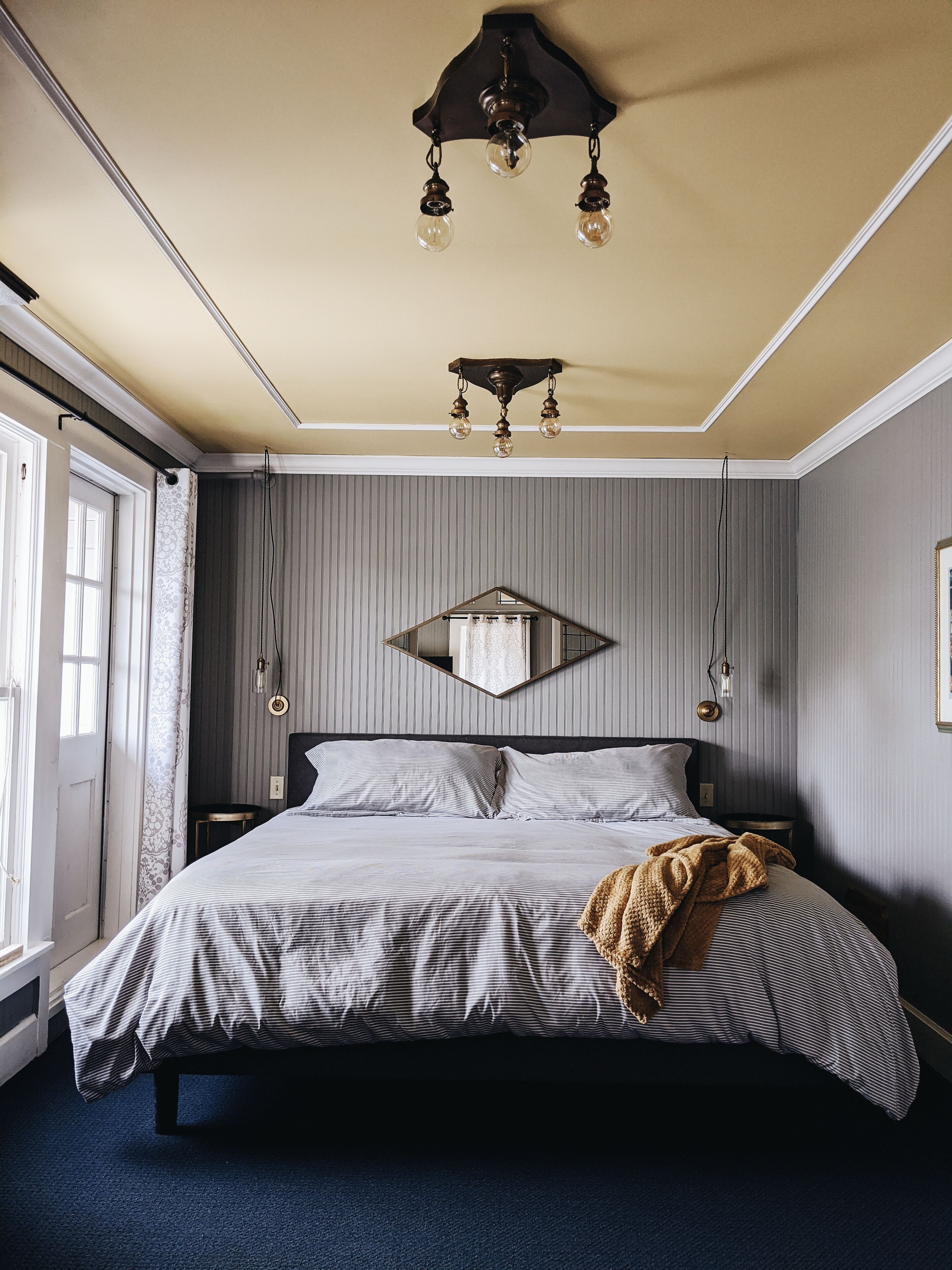Ein Schlafzimmer mit einem Bett, einer Deckenleuchte, einem Spiegel und einem Fenster.