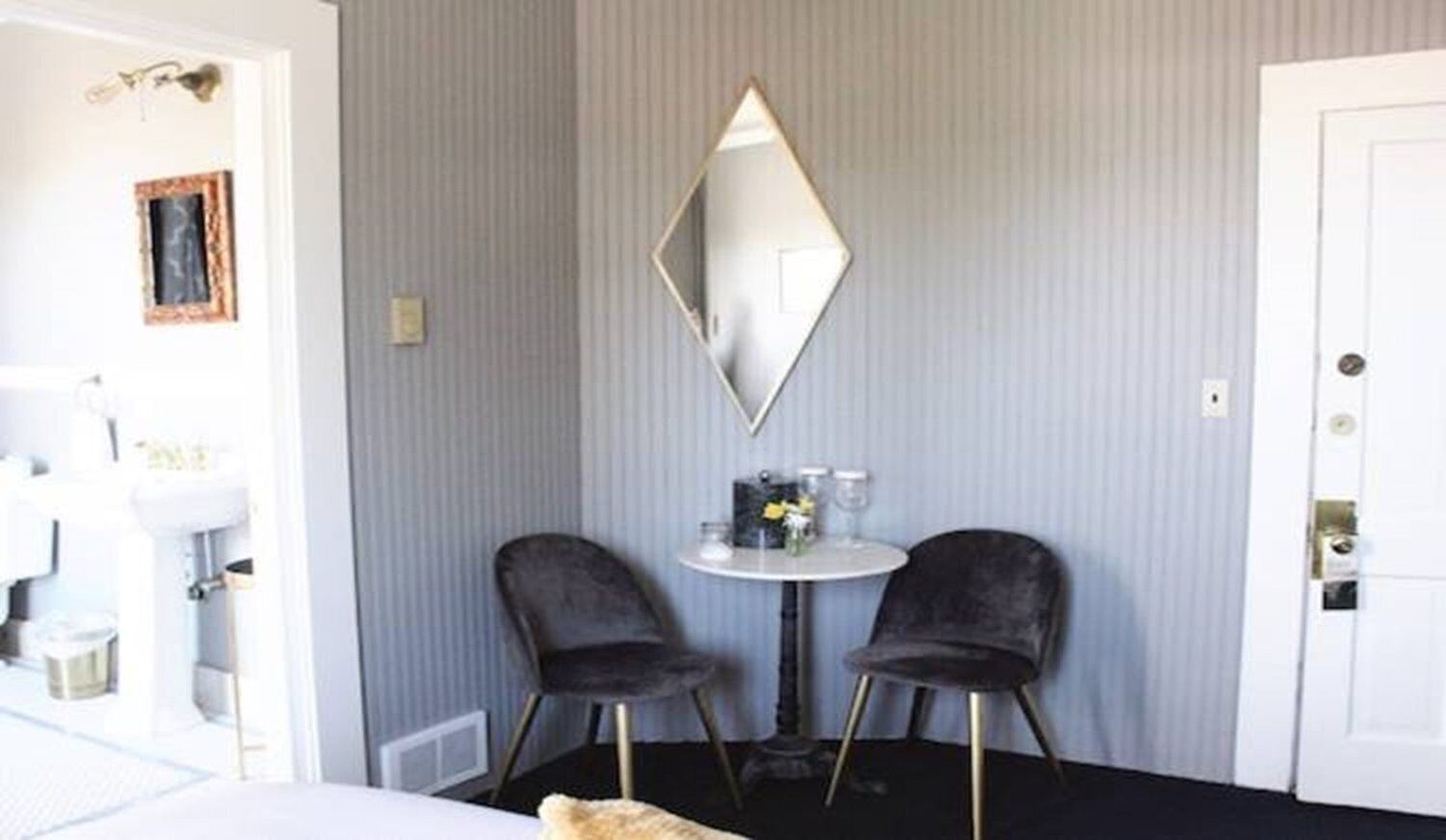 Una camera d'albergo con un letto, due sedie, un tavolino con un vaso e uno specchio a parete.