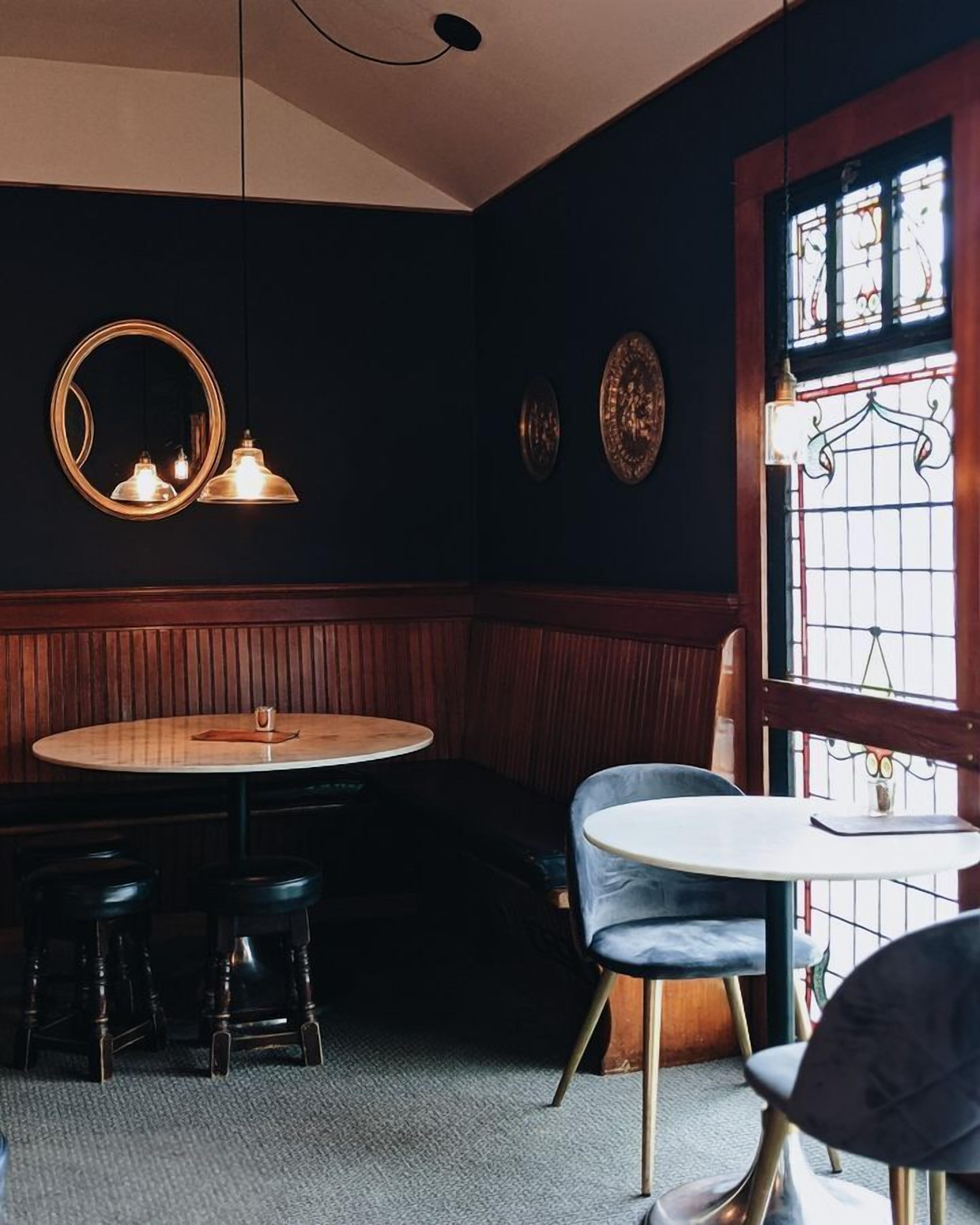 Interior acogedor de un restaurante con una mesa redonda, taburetes de bar y una pequeña mesa redonda con sillas.