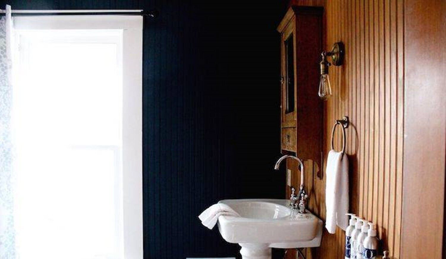 Un baño con un lavamanos blanco, un espejo y un perchero para toallas.