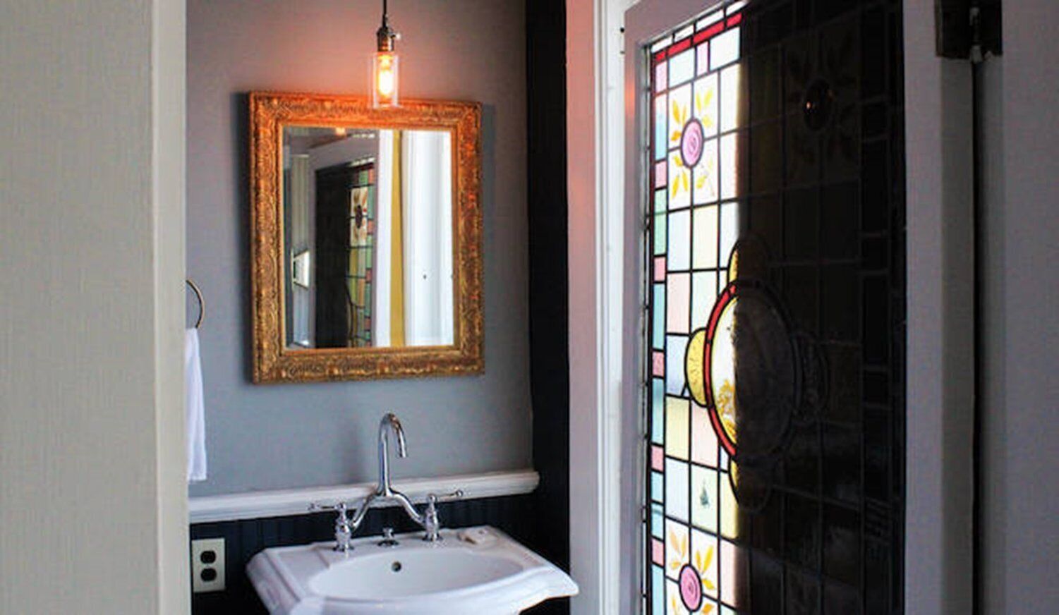 A bathroom with a white sink, a gold-framed mirror, and a stained glass door.