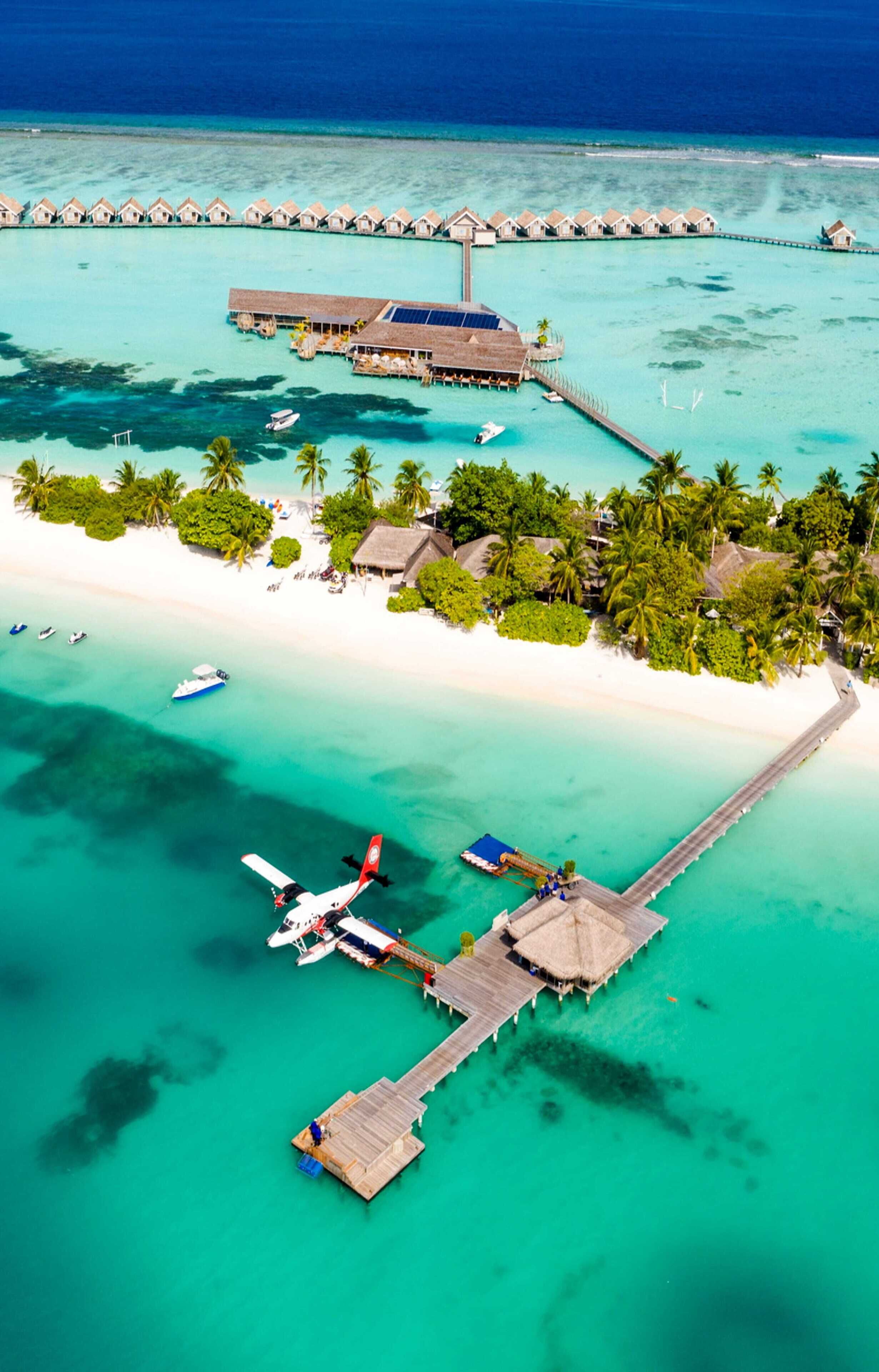 Luchtbeeld van een resort met bungalows op palen, een steiger en een klein vliegtuig.