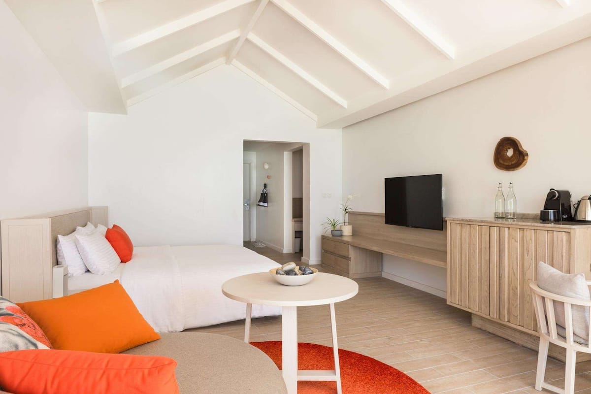 Ein modernes Hotelzimmer mit einem Bett, einem kleinen runden Tisch, einem Fernseher und einer Küchenzeile.