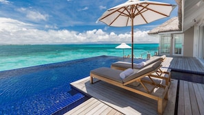 Una piscina infinita con sillones de playa y sombrillas, con vistas a aguas turquesas.