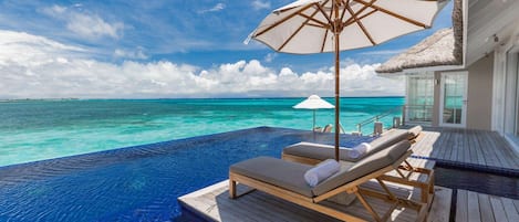 An infinity pool with lounge chairs and umbrellas, overlooking turquoise waters.