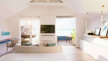 A modern bedroom with a large bed, a TV, and a balcony with a view of the sea.
