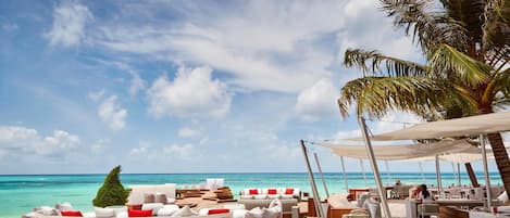 A beachside resort with outdoor seating, a bar, and a view of the ocean.