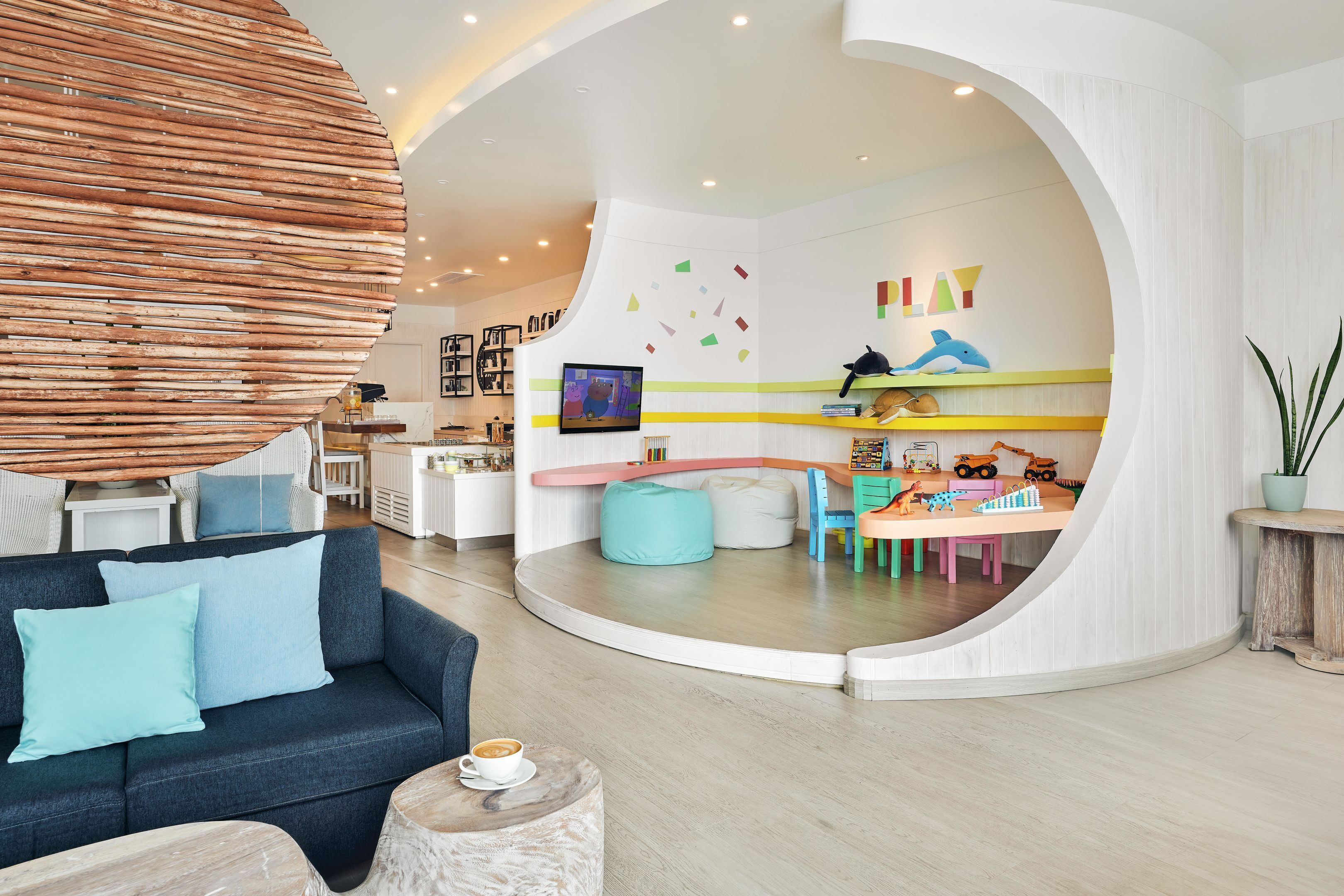 A modern living room with a curved wall, a sofa, a coffee table, and a play area with toys and a TV.