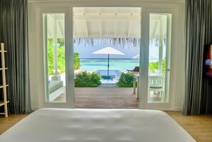 Une chambre avec un grand lit, une vue sur la piscine et une terrasse avec un fauteuil.
