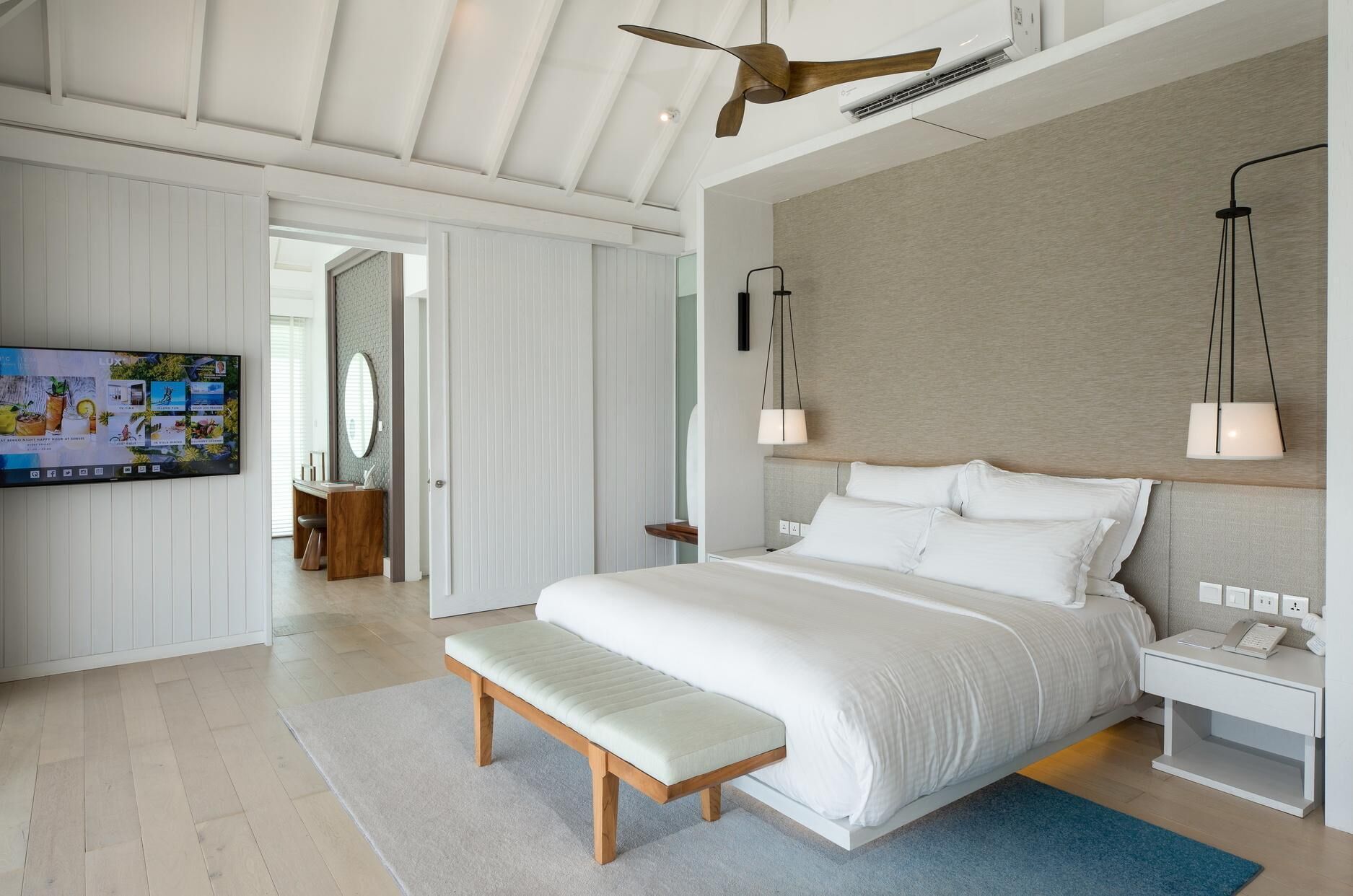 A modern hotel room with a large bed, a TV, and a ceiling fan.