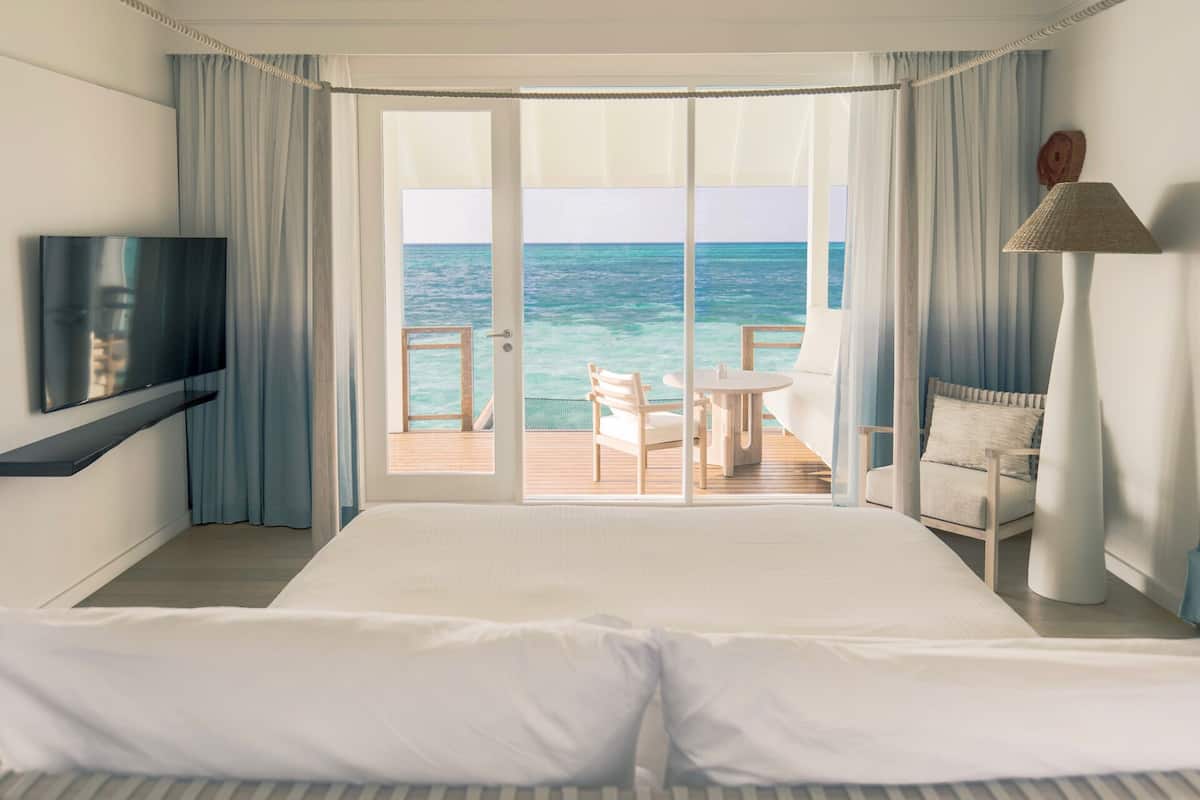 Ein Hotelzimmer mit einem großen Bett, einem Fernseher, einem Balkon mit Meerblick und einem Tisch mit Stühlen.