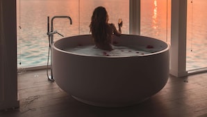 Una persona en una bañera disfrutando de la vista del atardecer sobre el mar.