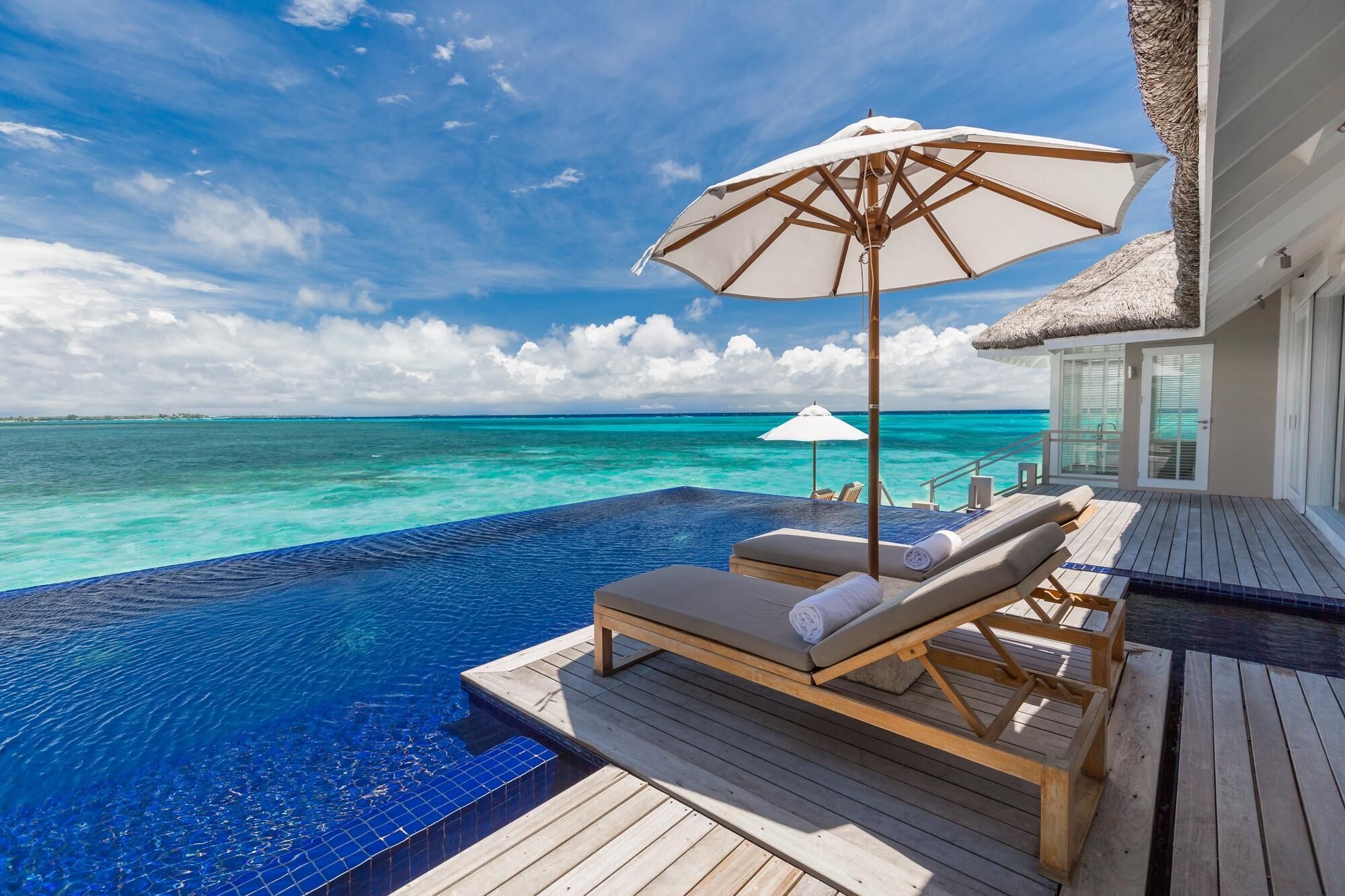 Une piscine à débordement avec des chaises longues et des parasols, offrant une vue sur des eaux turquoise.