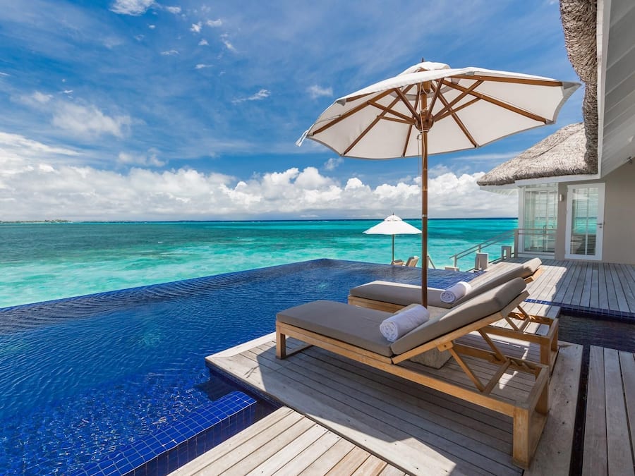 Une piscine à débordement avec des chaises longues et des parasols, offrant une vue sur des eaux turquoise.