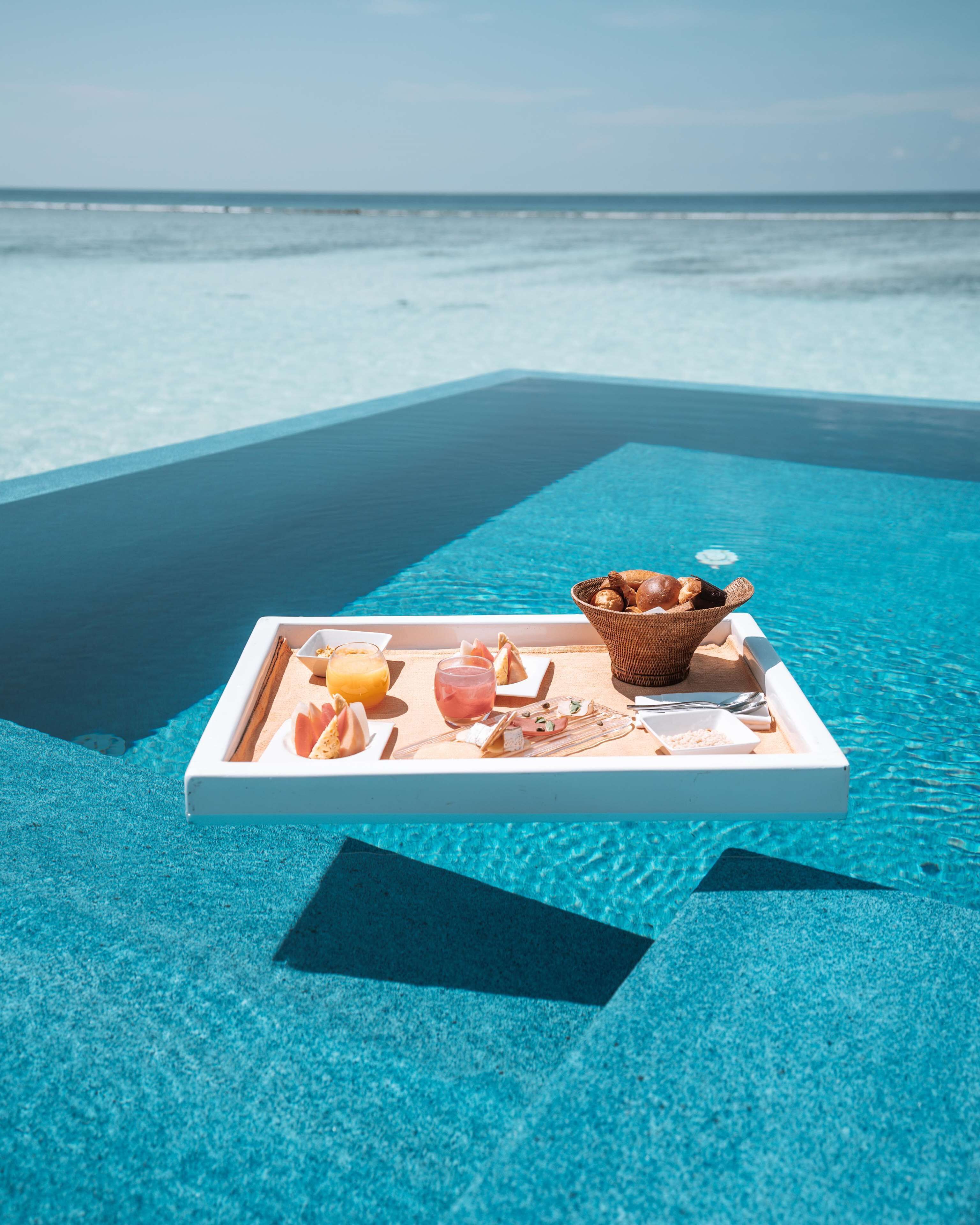 A tray with food and drinks on a poolside deck with a view of the ocean.