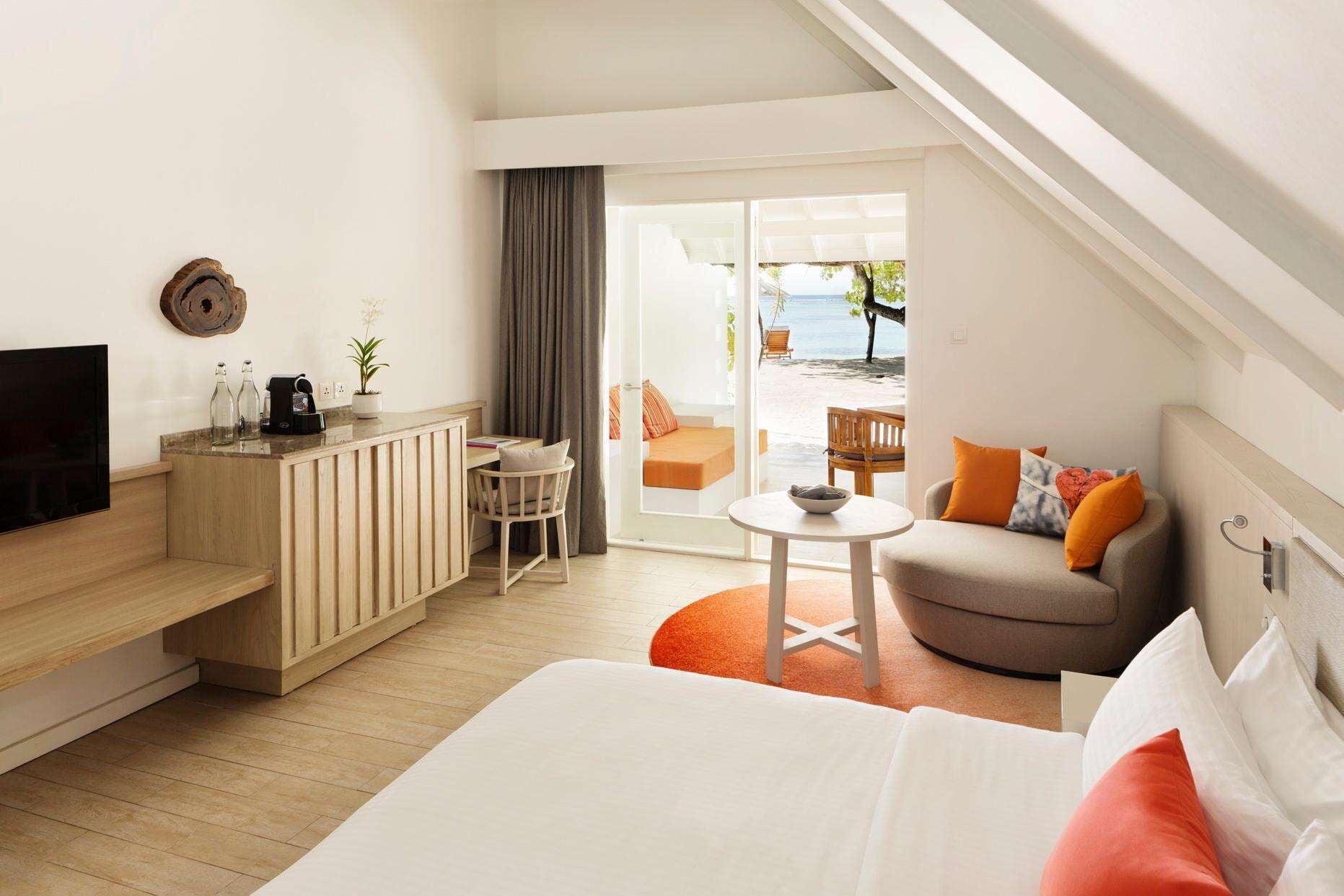 A hotel room with a bed, a desk, a TV, a chair, a sofa, and a view of the beach.