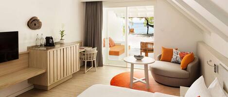 A hotel room with a bed, a desk, a TV, a chair, a sofa, and a view of the beach.