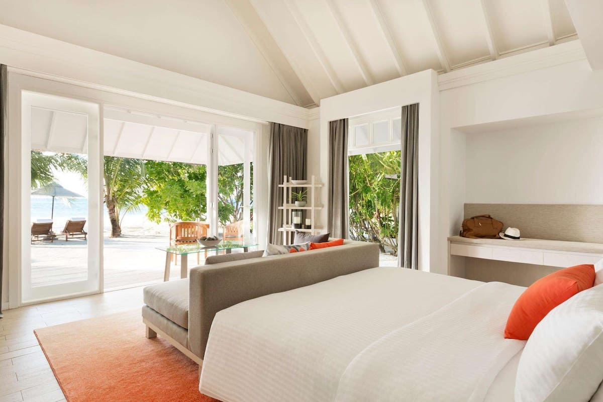 Ein Hotelzimmer mit Bett, einer Sitzecke mit Tisch und Blick auf den Strand.