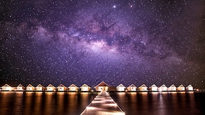 Cielo estrellado sobre un muelle de madera que conduce a bungalows sobre el agua.