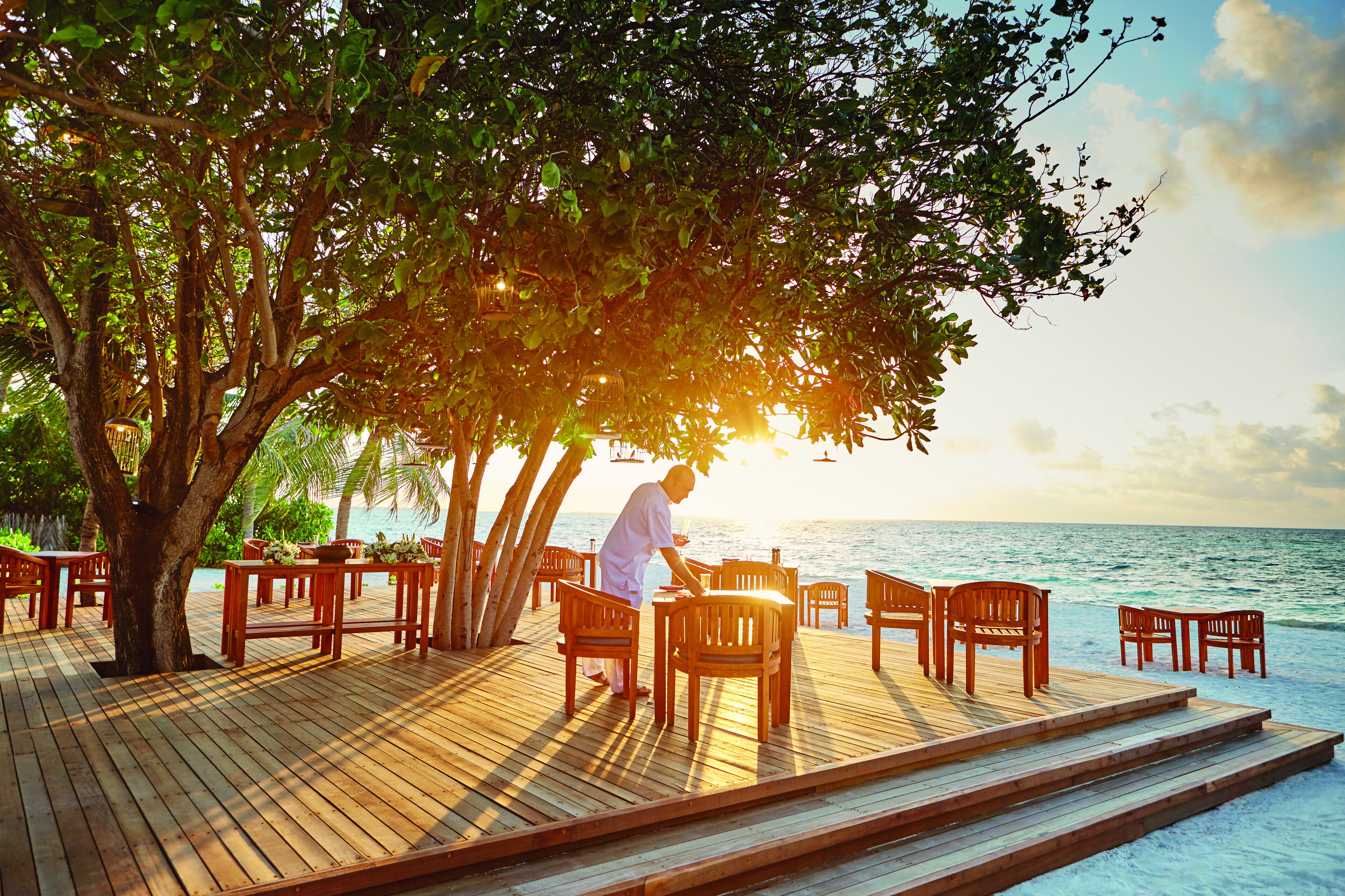 A wooden deck with tables and chairs, overlooking a body of water.