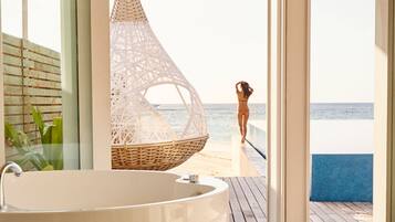 A modern bathroom with a large bathtub, a wicker hanging chair, and a view of the beach.