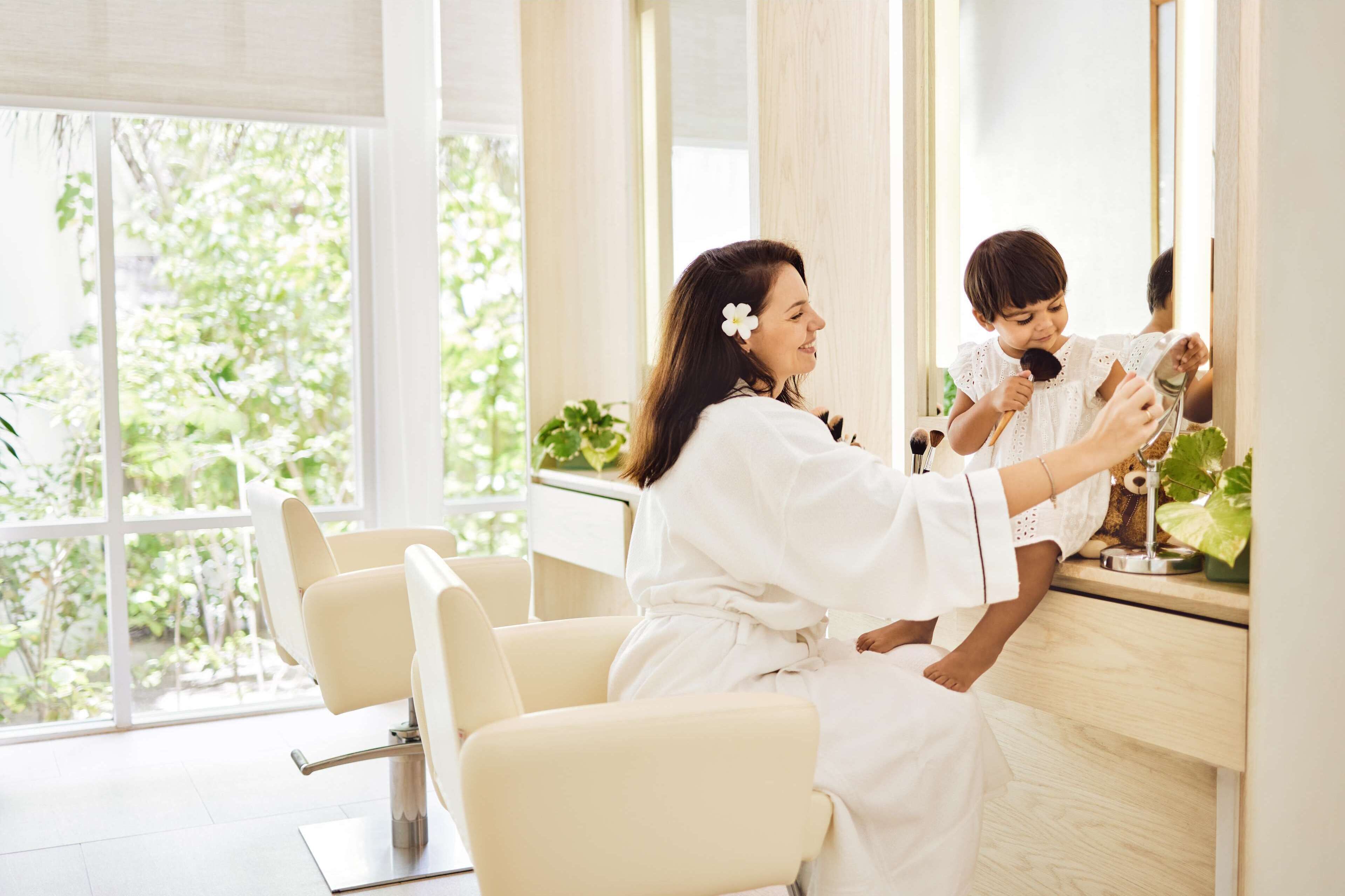 A person in a white robe sitting at a counter with a mirror, holding a small object.