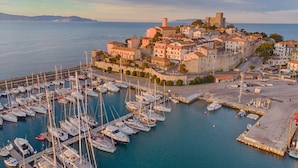 Un pueblo costero con un puerto deportivo lleno de barcos, edificios históricos y un castillo imponente en una colina.