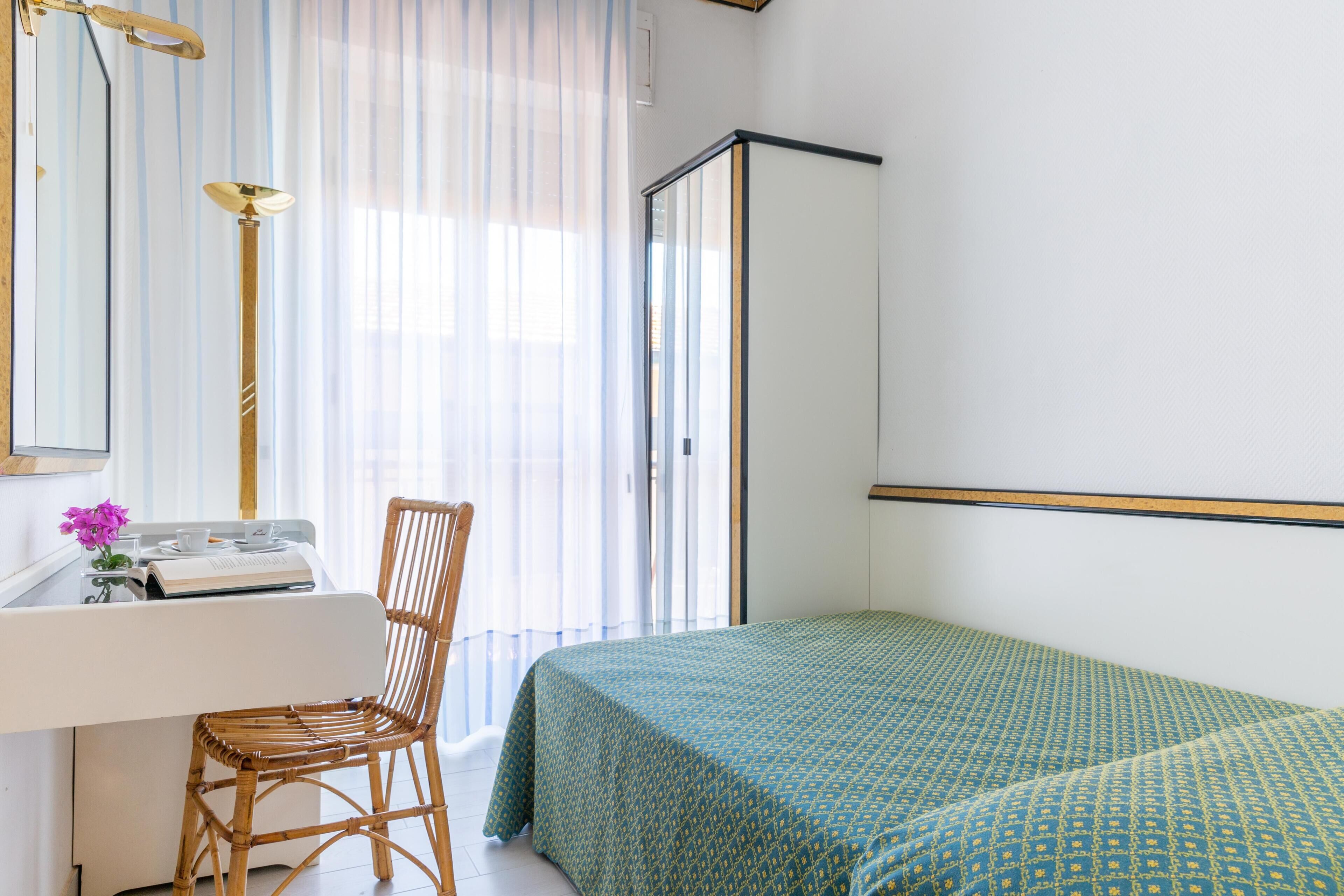 A bedroom with a bed, a chair, a desk with a lamp, and a window with curtains.