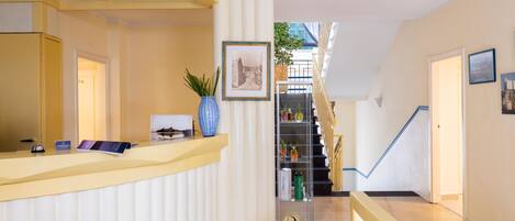 A reception area with a counter, framed picture, potted plant, and a staircase leading to an upper level.