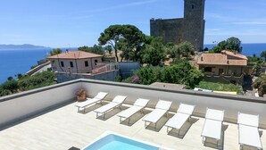 Zona de piscina en la azotea con sillones de descanso y vistas a un castillo y al mar.