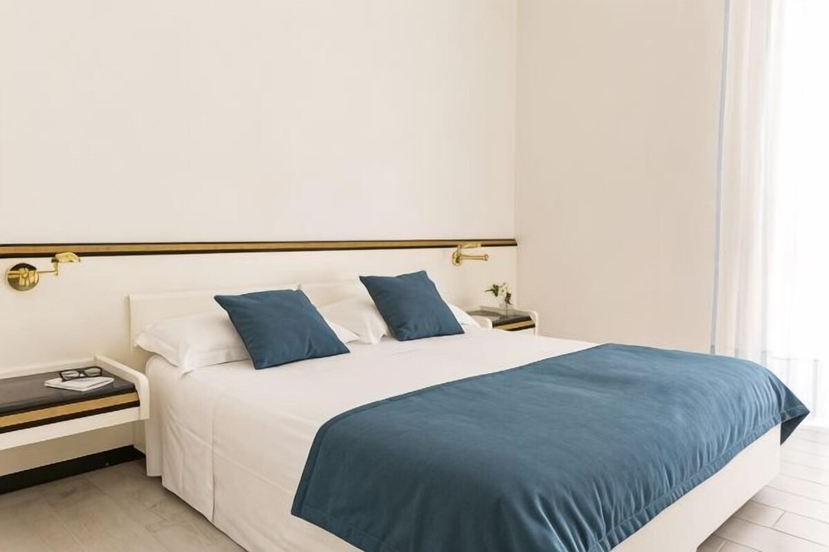 Una habitación de hotel con una cama, dos mesitas de noche y una mesita auxiliar.