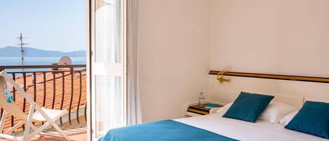 A bedroom with a bed, a nightstand, and a chair. The room has a view of the sea and mountains.