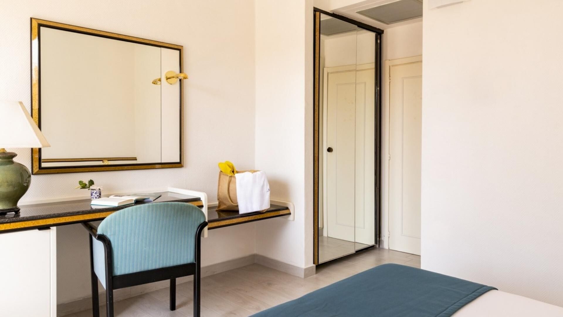 Ein Hotelzimmer mit Schreibtisch, Stuhl, Bett, Spiegel und einer Tür zu einem Badezimmer.