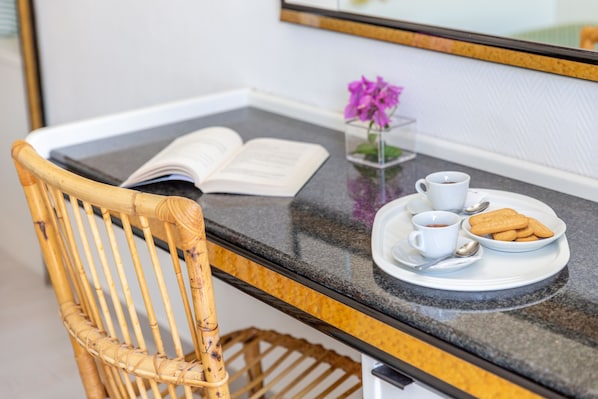 Una silla de mimbre, una bandeja con un libro, una taza de café, un plato de galletas y un pequeño florero con flores sobre una encimera.
