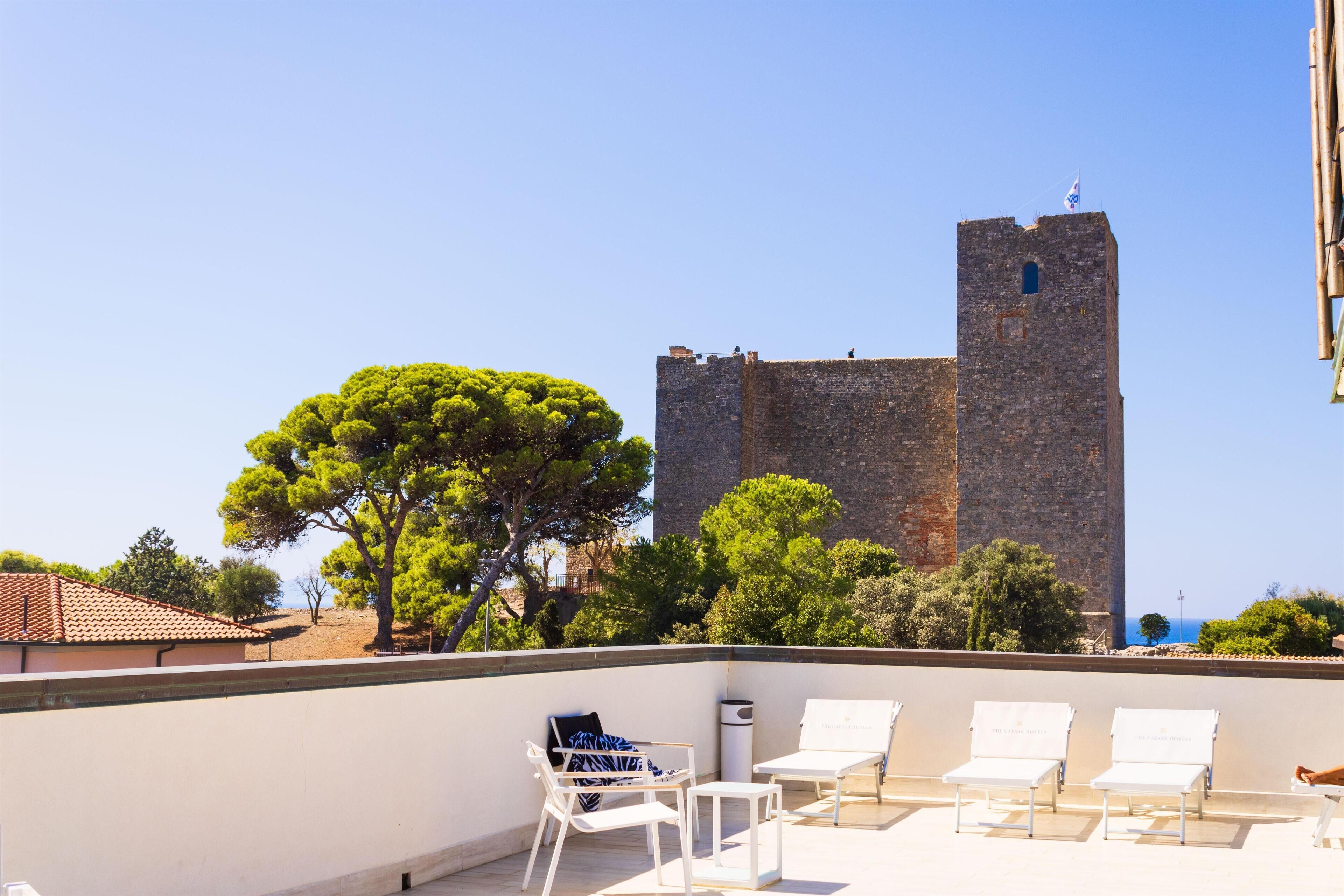 Terraza en la azotea con sillones blancos y vista a una torre de piedra histórica.