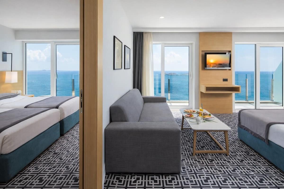 Une chambre d’hôtel avec un grand lit, un canapé, une petite table avec le petit-déjeuner et une télévision.