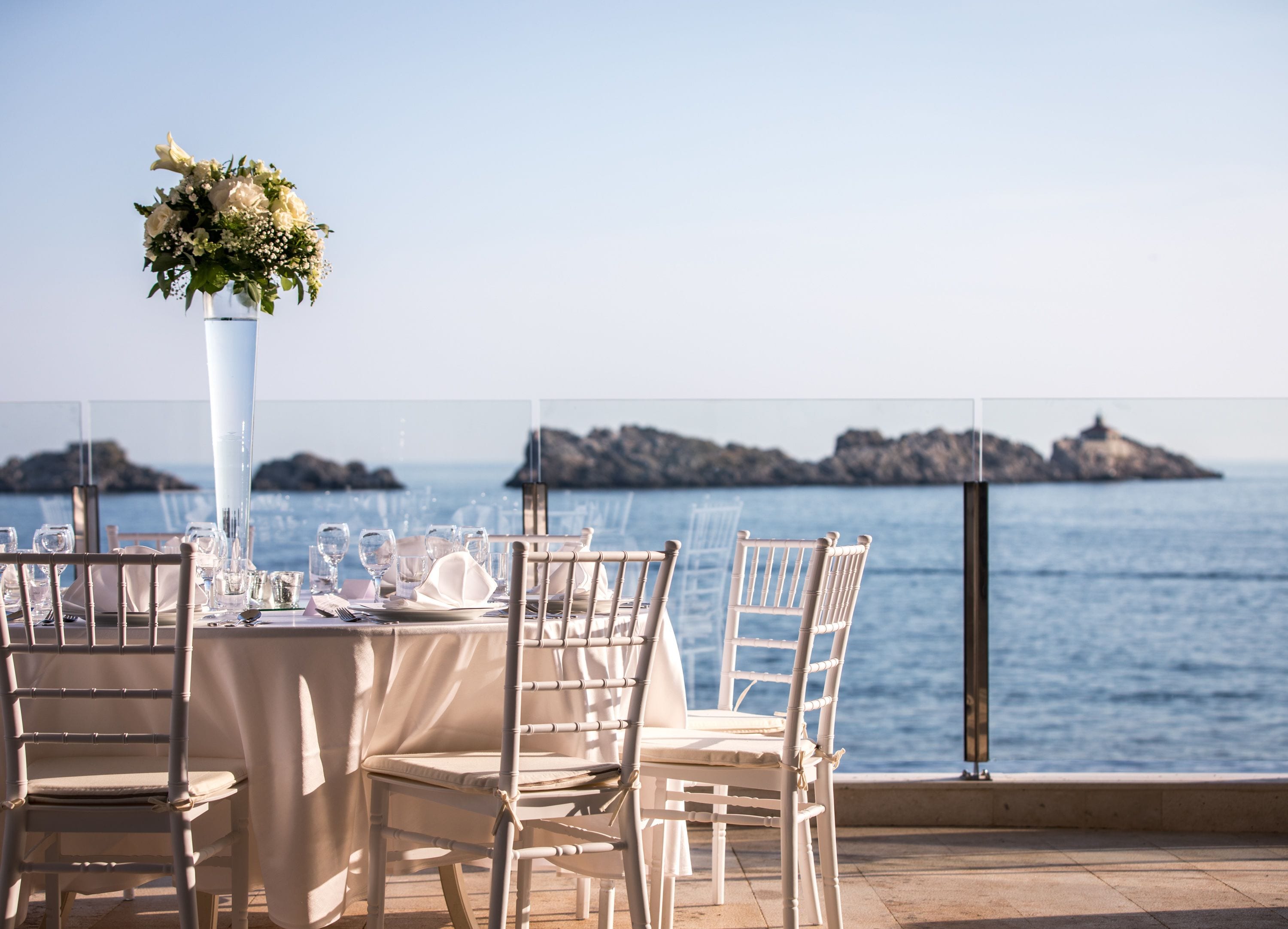 A table set for dining with a view of the sea and rocky outcrops.