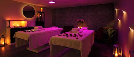 A spa room with two massage tables, candles, and a mirror.