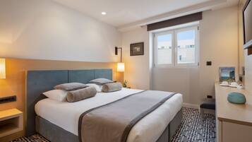 Habitación de hotel con una cama grande, mesitas de noche, un escritorio con silla, una ventana y vistas a edificios.