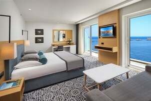 Quarto de hotel moderno com uma cama grande, uma escrivaninha, televisão e vista para o mar.