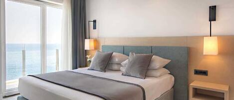Une chambre d’hôtel avec un grand lit, une table de chevet, une lampe fixée au mur et une vue sur la mer.